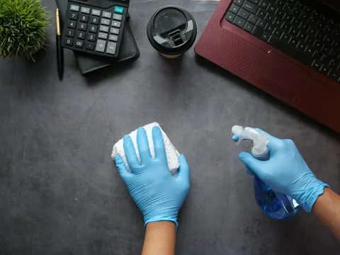 Schreibtisch im Büro wird mit Handschuhen und Tuch gereinigt